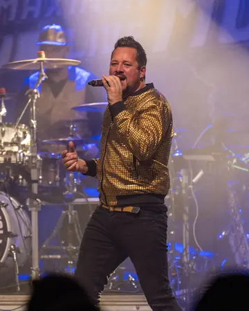 Alexander Lühr singt in goldener Jacke auf einer Konzertbühne.