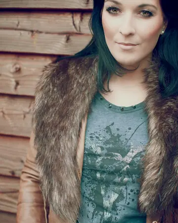 Christina Maria Brenner mit Fellkragen vor einer Holzwand