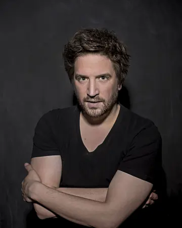 Florian Hinxlage mit verschränkten Armen vor dunklem Hintergrund.