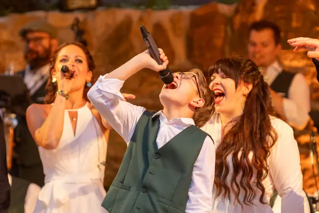 Zwei Sängerinnen und ein junger Sänger singen gemeinsam im warmen Bühnenlicht.