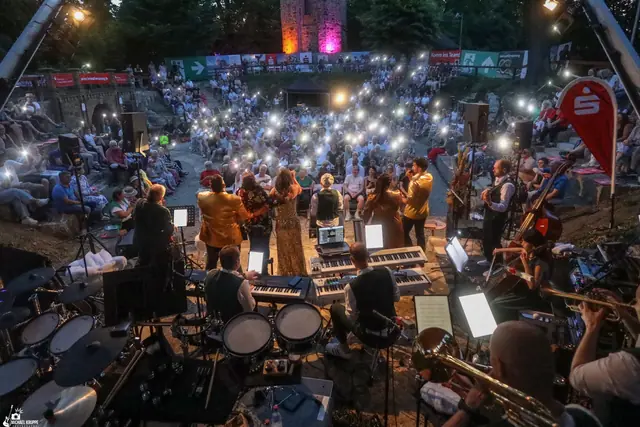 Blick über die Band auf das Publikum in der Dämmerung: Hunderte Handylichter leuchten, hinten der angestrahlte Klütturm.