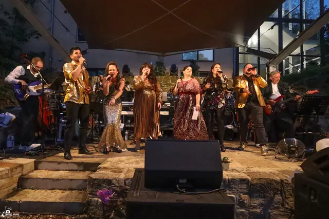 Sängerinnen und Sänger in Gold und Glitzer singen gemeinsam auf der Bühne, hinter ihnen die Band.