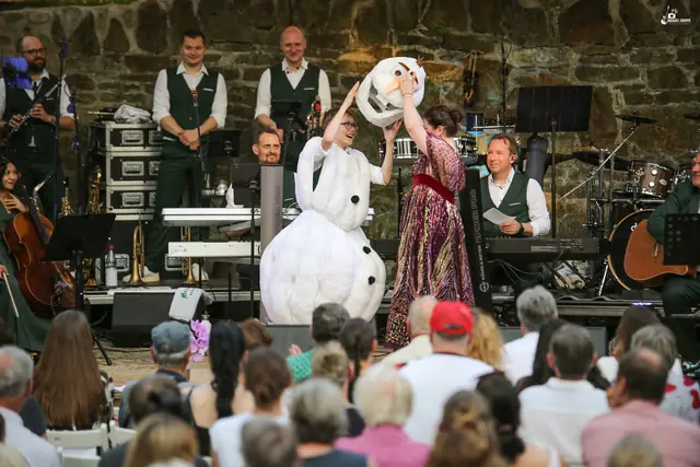 Ein Schneemann-Kostüm wie aus „Die Eiskönigin“ auf der Bühne, daneben eine Sängerin, dahinter die Band.