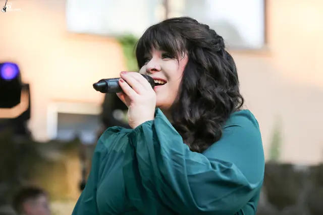 Eine Sängerin im dunkelgrünen Kleid singt lächelnd ins Mikrofon.
