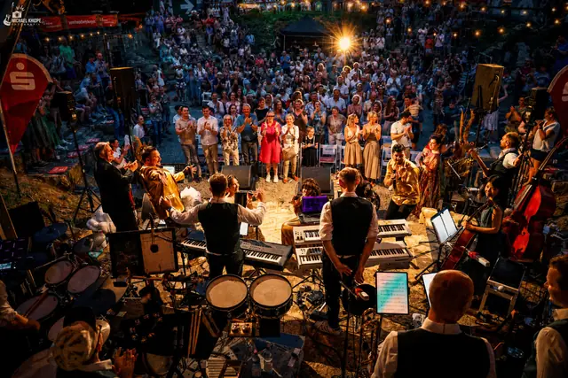Finale in der Dämmerung: Das Ensemble steht vor der Band, die Ränge dahinter sind voll besetzt.