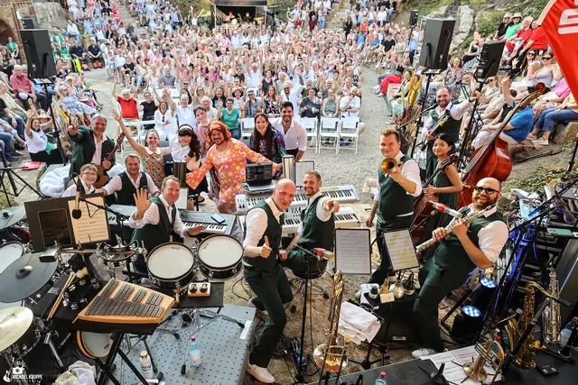 Die Band dreht sich zur Kamera und winkt, dahinter jubelt das Publikum.