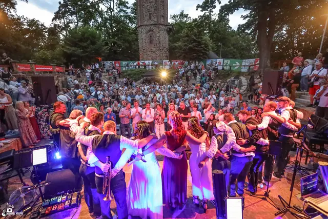 Blick von der Bühne über das voll besetzte Rund der Waldbühne, hinten der Klütturm. Das Ensemble steht Arm in Arm im Kreis.